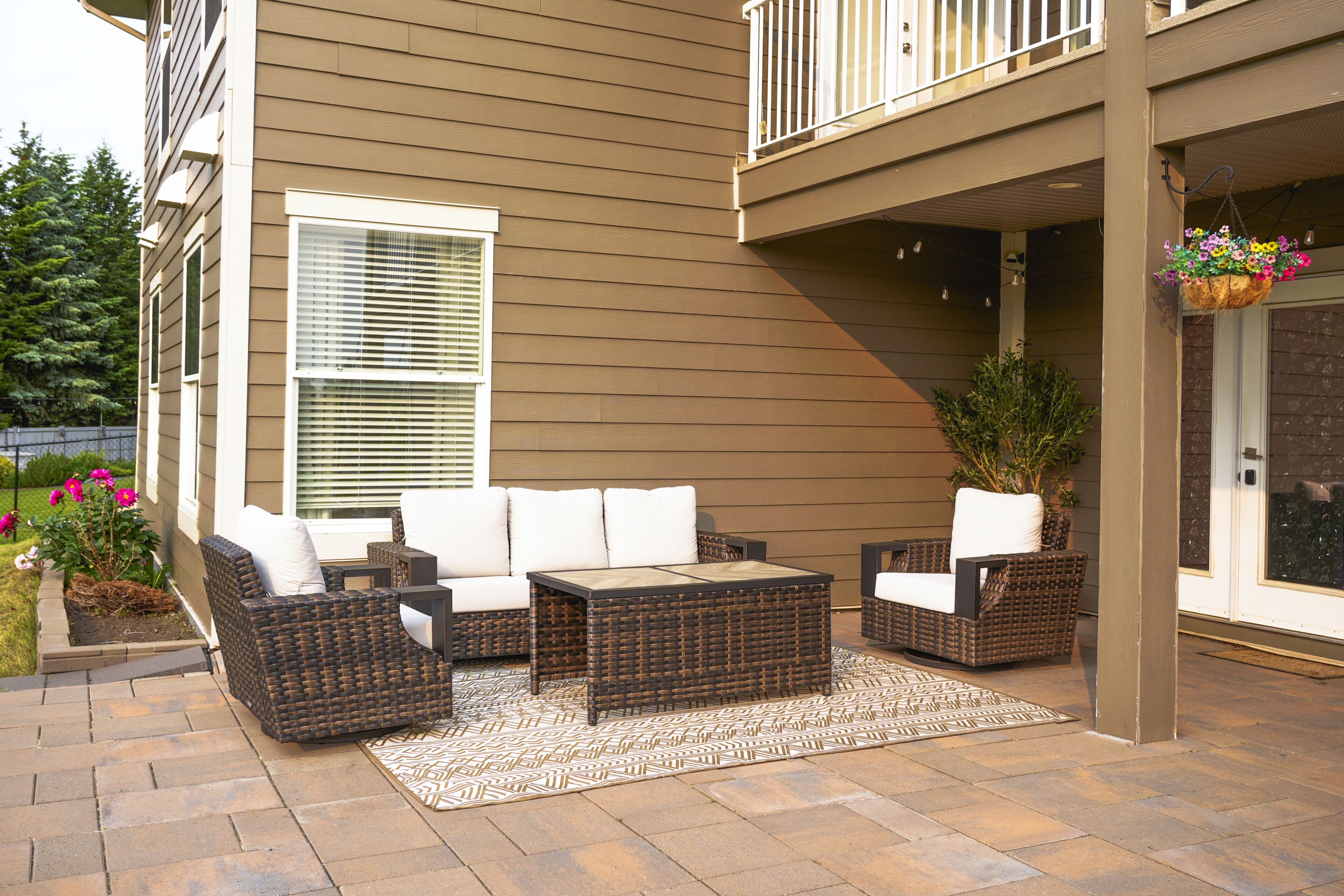 Une terrasse extérieure avec des meubles en osier, un tapis à motifs et une jardinière suspendue.