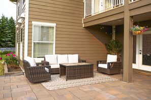 Eine Terrassenausstattung mit Korbmöbeln, einem gemusterten Teppich und einem hängenden Blumentopf.