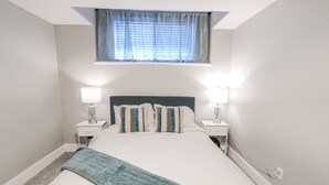A bedroom with a bed, two bedside tables with lamps, a window with curtains, and a carpeted floor. - 4BR Dream Family Stay! ☆ King Bed / Home Theatre / Large Backyard ☆ Pet Friendly (Sturgeon County)