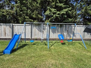 Un parque infantil con tobogán, columpios y un conjunto de columpios.