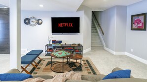 A living room with a flat-screen TV mounted on the wall, a coffee table, a sofa, and a staircase leading upstairs. - 4BR Dream Family Stay! ☆ King Bed / Home Theatre / Large Backyard ☆ Pet Friendly (Sturgeon County)