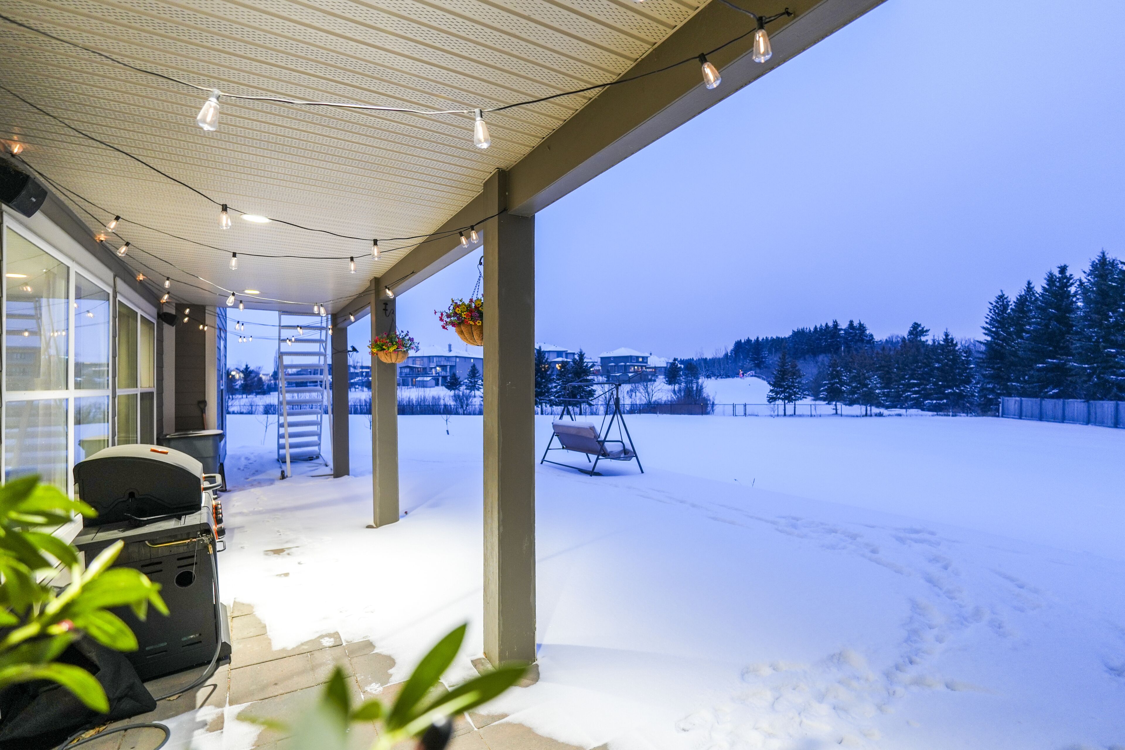 A covered outdoor area with a snow-covered ground, a swing, and hanging flower baskets.