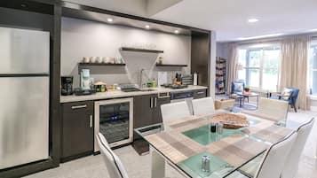 Een moderne keuken met een inbouwvaatwasser, koffiezetapparaat en magnetron. Er is een eettafel met stoelen en een raam met gordijnen.
