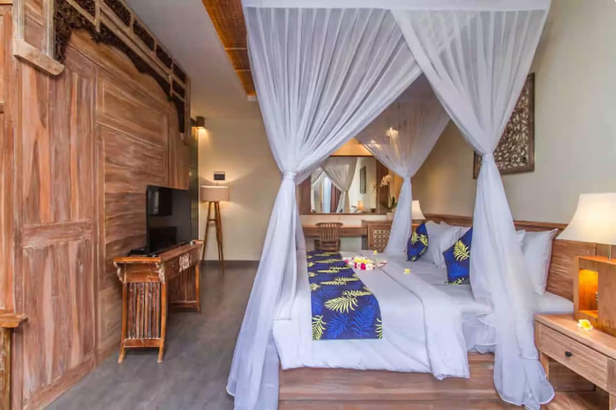 A bedroom with a four-poster bed, a television, a desk, and a mirror.