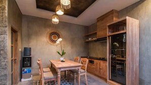 Ein Essbereich mit Holztisch und -stühlen, einem Wasserspender, einem Wandbehang und einer Küchenzeile mit Holzausbau und Kühlschrank.
