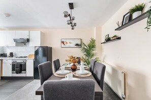 A modern kitchen with white cabinets, a black refrigerator, and a dining area with a table set for four. - Cozy House w/garden near 02 Arena sleeps 10, 2 mins to station (London)