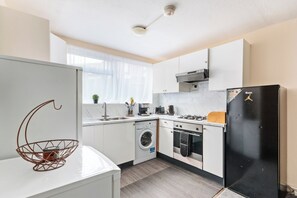 A modern kitchen with white cabinetry, a black refrigerator, a built-in oven, and a washing machine. - Cozy House w/garden near 02 Arena sleeps 10, 2 mins to station (London)
