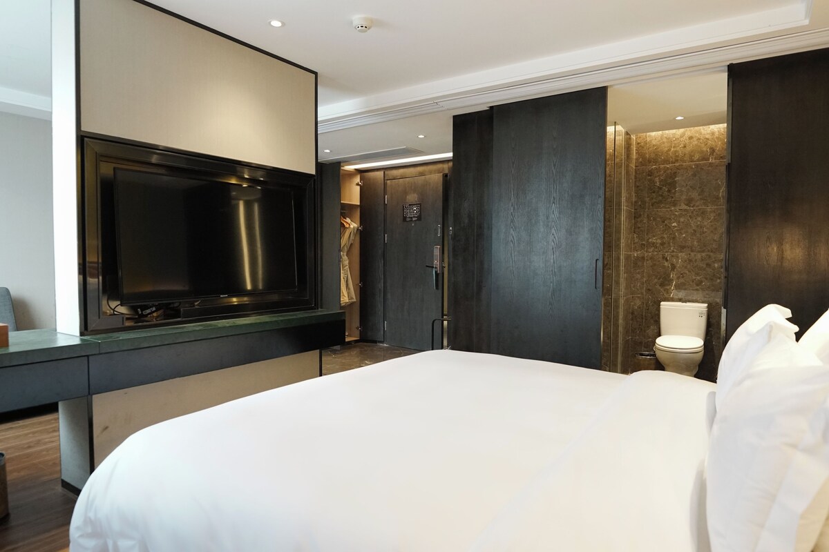 A modern hotel room with a large bed, a flat-screen TV, a walk-in closet, and a bathroom with a marble shower.