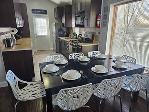 A modern kitchen with dark cabinetry, a central island, and a dining area with white chairs and a black table set for four. - 5 Bedroom, 3 Baths, 2 Living Rooms, Super Comfortable Home in Ypsilanti (Ypsilanti)