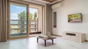 A modern room with a sliding glass door, a table with a book and a cup, a TV, and a painting on the wall.