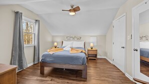 Een slaapkamer met een bed, nachtkastjes, een plafondventilator en een raam met gordijnen.