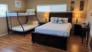 A bedroom with a bunk bed, a single bed, wooden flooring, two bedside lamps, and artwork on the walls. - Spacious 5-bedroom house in terrific San Diego with AC (San Diego)