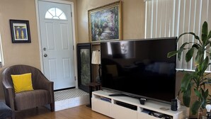 A living room with a flat-screen TV on a white stand, a ceiling fan, a door, and a potted plant. - Spacious 5-bedroom house in terrific San Diego with AC (San Diego)