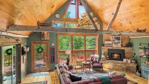Ein gemütliches Blockhaus-Interieur mit Holzbalkendecke, großen Fenstern, einem Kamin und einer komfortablen Sitzecke.