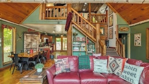 Ein rustikales Cabin-Interieur mit Essbereich, einer roten Ledersofa und dekorativen Kissen sowie einer Holztreppe.