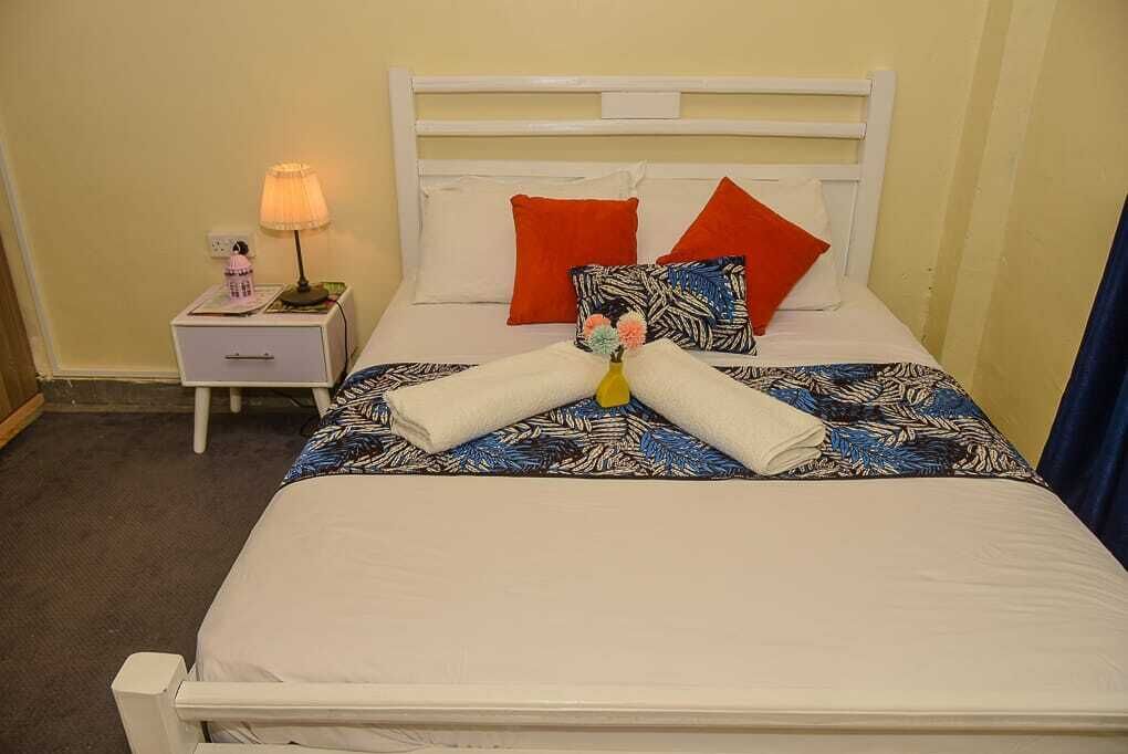 A neatly made bed with a patterned bedspread, two red pillows, and a white headboard.
