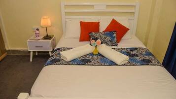 A neatly made bed with a patterned bedspread, two red pillows, and a white headboard.
