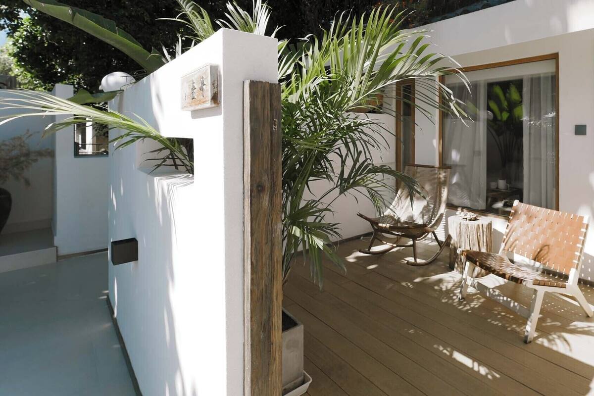 Un espacio al aire libre con techo, que cuenta con una terraza de madera, una mecedora y un sofá.