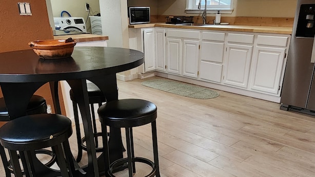 A modern kitchen with white cabinets, a black countertop, and a stainless steel refrigerator. There is a round table with two black stools. - Cute Parkside House (Grants Pass)