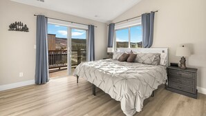 Ein Schlafzimmer mit einem großen Bett, einem Nachttisch, einem Fenster mit Vorhängen und Blick ins Freie.