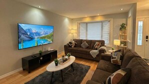 Ett vardagsrum med en stor TV med platt skärm, en mörkbrun soffa, ett soffbord och en bokhylla.