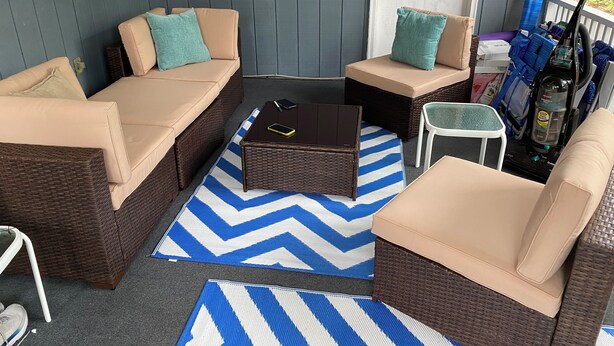 A covered porch with wicker furniture, a blue and white chevron rug, and a blue water bottle. - Exceptional Dewey Beach Stay Central Location Near Ocean & Bay (Dewey Beach)