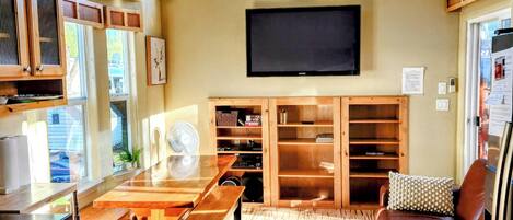 Un amplio espacio de sala con piso de madera, ventilador de techo, televisor de pantalla plana, estanterías empotradas, un banco de madera y un sofá de cuero.