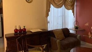 Uma sala de estar com um sofá castanho, uma escrivaninha de madeira com uma lâmpada e uma janela com cortinas.