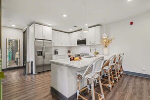 A modern kitchen with white cabinets, stainless steel appliances, and a central island with wicker chairs. - Petal & Palm-Rooftop Patio & Gym-Mins to Broadway (Nashville)