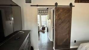 A bedroom with a large bed, a dresser, and a sliding barn-style door leading to a hallway. - Welcome to Your Lakefront Retreat (Osage Beach)