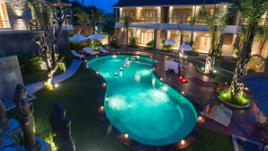 Una piscina dalla forma sinuosa, circondata da lettini e ombrelloni, con un edificio sullo sfondo.