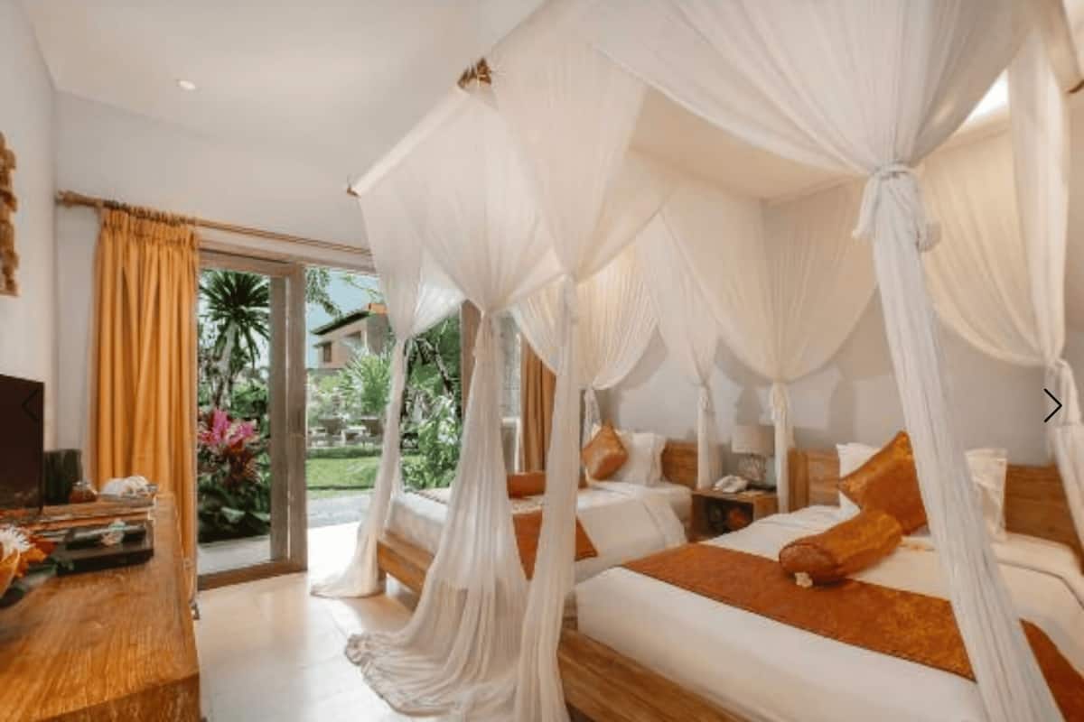 A room with a four-poster bed, a wooden desk, and a large window with curtains.