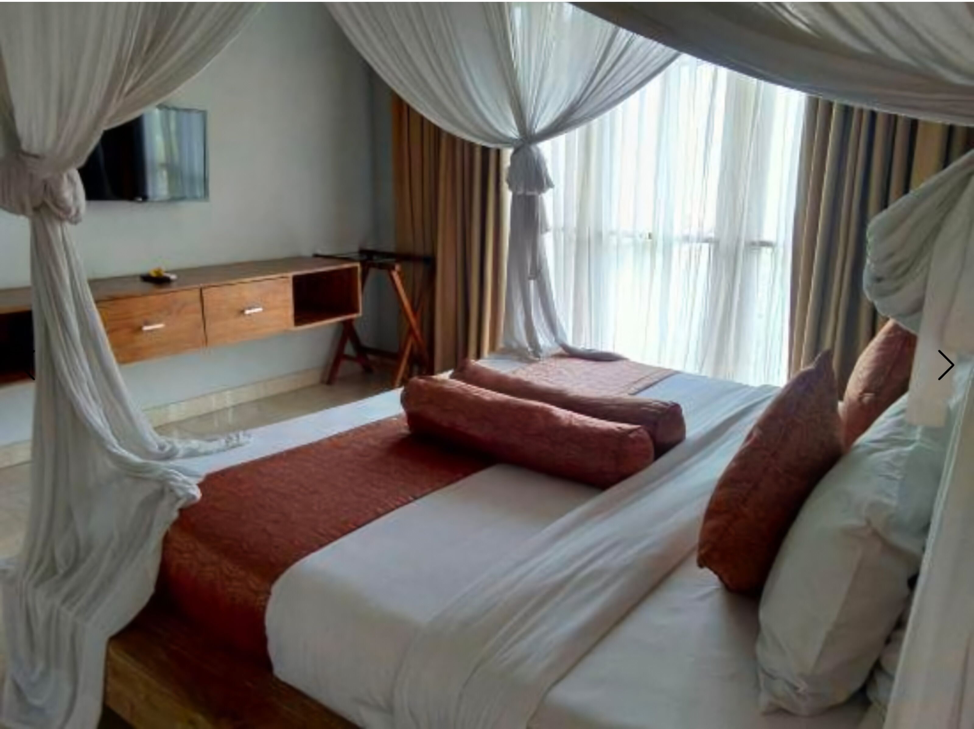 A bedroom with a bed, a desk, and a TV on the wall.