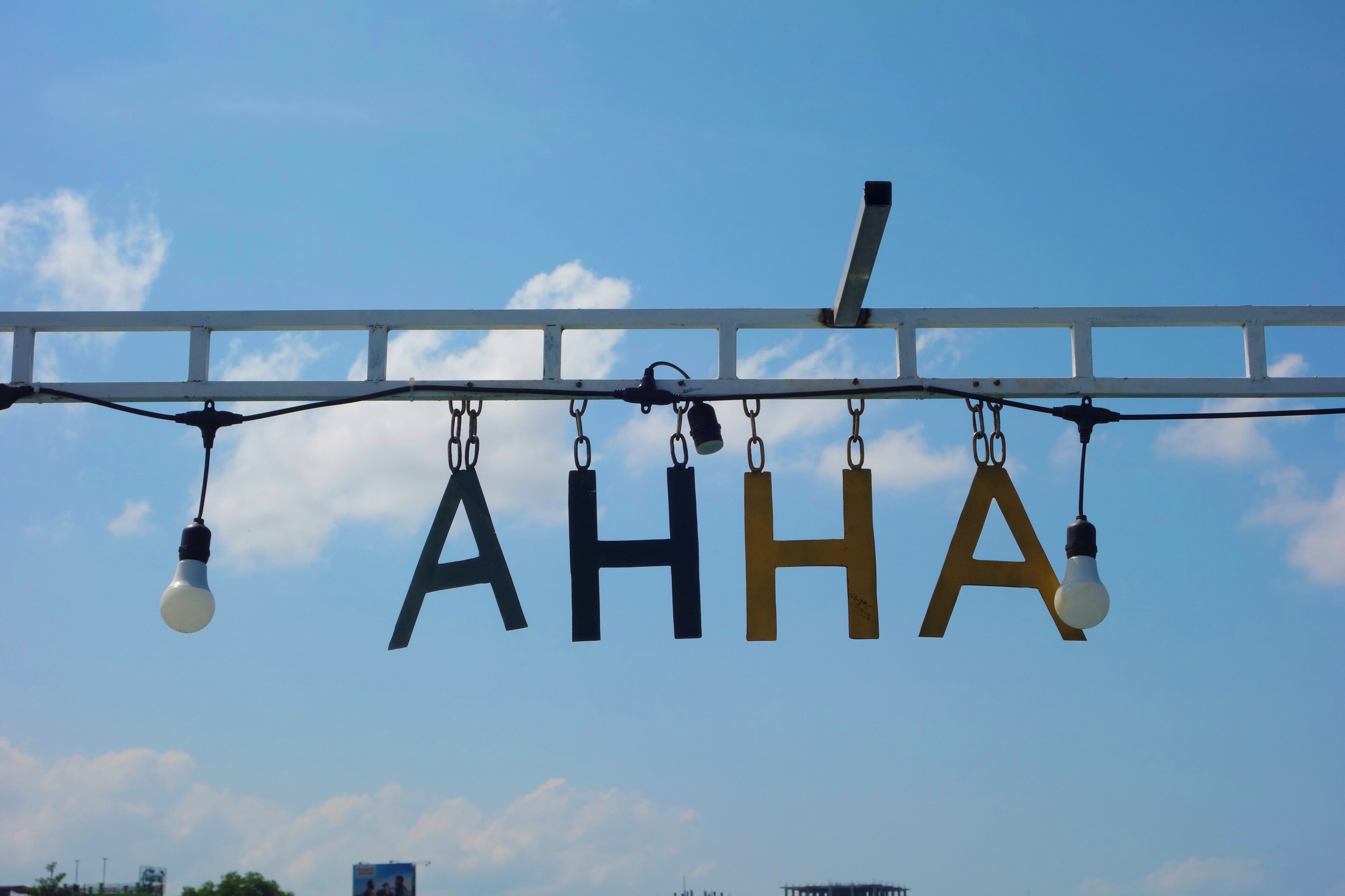 Une structure métallique dont pendent les lettres « AHHA », chaque lettre étant suspendue à une chaîne et éclairée par une ampoule.