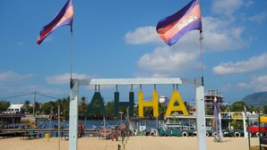 A beach with flags, a sign with letters, and boats in the background. - AHHA Floatel Kampot (Santuk)