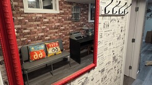 Una habitación con pared de ladrillo, un cartel de Route 66, un espejo con marco rojo, un banco con cojines de colores y un escritorio con lámpara.