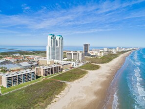 A coastal cityscape with a beachfront hotel featuring multiple buildings, a beach, and a pier in the background. - Sapphire #704 | Beachfront Condo • Gulf & Bay Views • Resort Pool (South Padre Island)