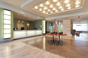 A hotel lobby with a reception desk, a round table with vases, and a stone pillar. - Sapphire #704 | Beachfront Condo • Gulf & Bay Views • Resort Pool (South Padre Island)