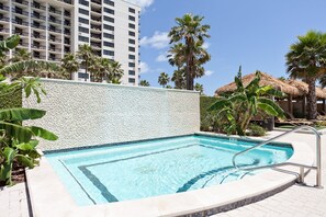 Una piscina con borde de azulejos, rodeada de palmeras y un rascacielos al fondo.