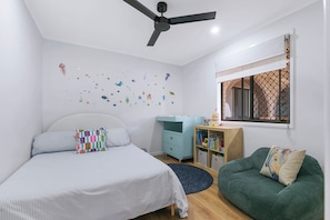A bedroom with a bed, a green sofa, a desk with books, a ceiling fan, and a window with a view. - Entire home in Kippa-Ring, Australia (Kippa-Ring)