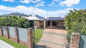 A residential property with a gated driveway, solar panels on the roof, and a covered patio area.