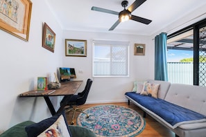 A room with a ceiling fan, a desk with a computer, a sofa, and a window with a view. - Entire home in Kippa-Ring, Australia (Kippa-Ring)
