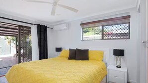 A bedroom with a bed, a ceiling fan, a window with a view, and an air conditioning unit.