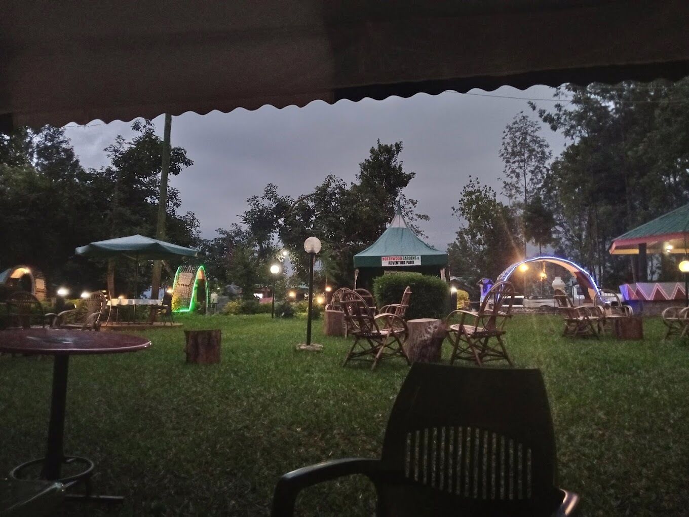 Un espacio al aire libre con mesas y sillas, rodeado de árboles y una carpa con el letrero "Adventure Park".