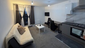 Ein kompakter Wohnbereich mit Sofa, Esstisch, Fernseher und Küchenzeile mit Herd.