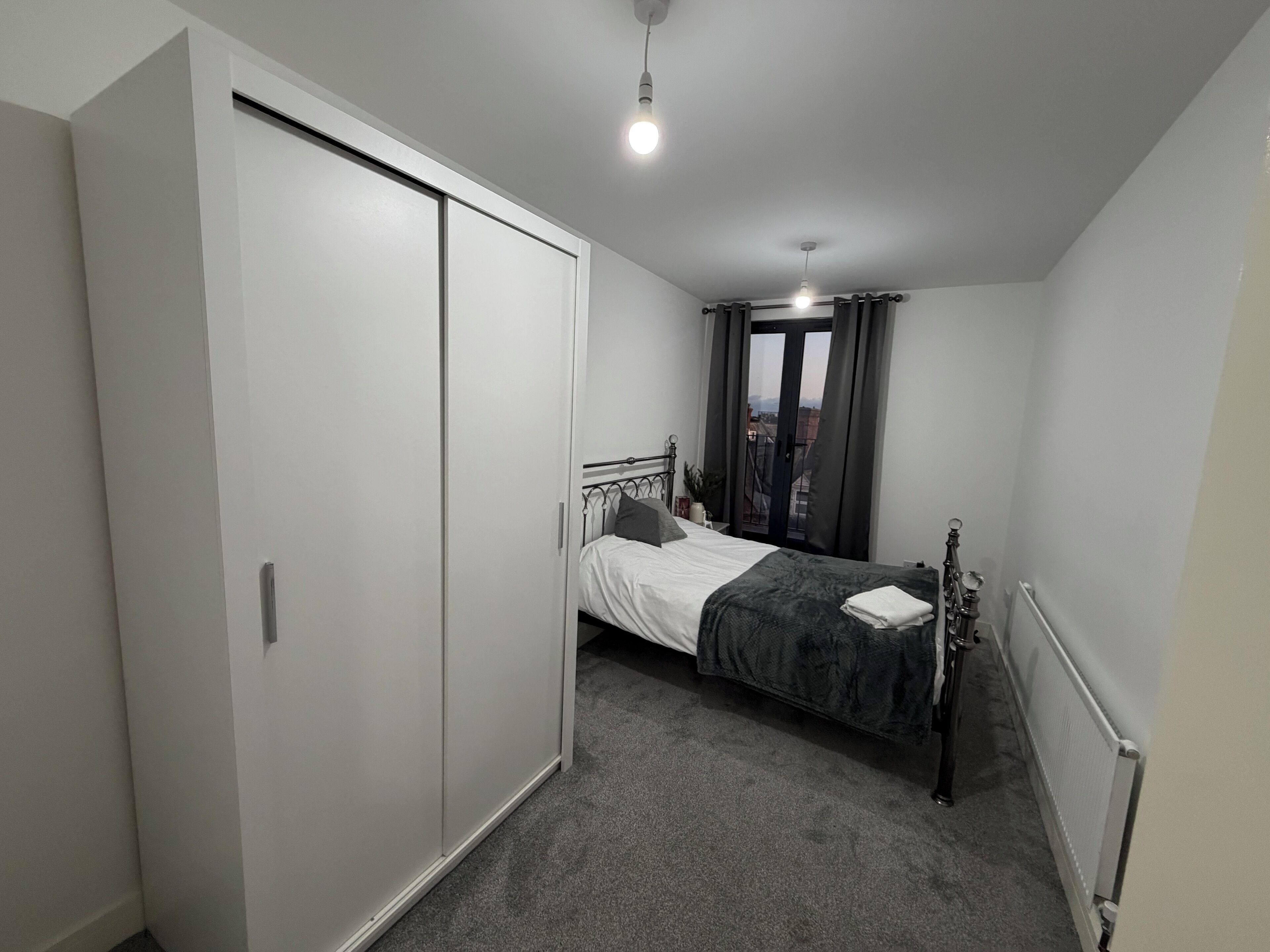 A bedroom with a bed, a wardrobe, a radiator, and a window with curtains.