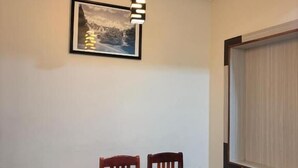 Een eethoek met een houten tafel en stoelen, een hanglamp en een ingelijst schilderij aan de muur.