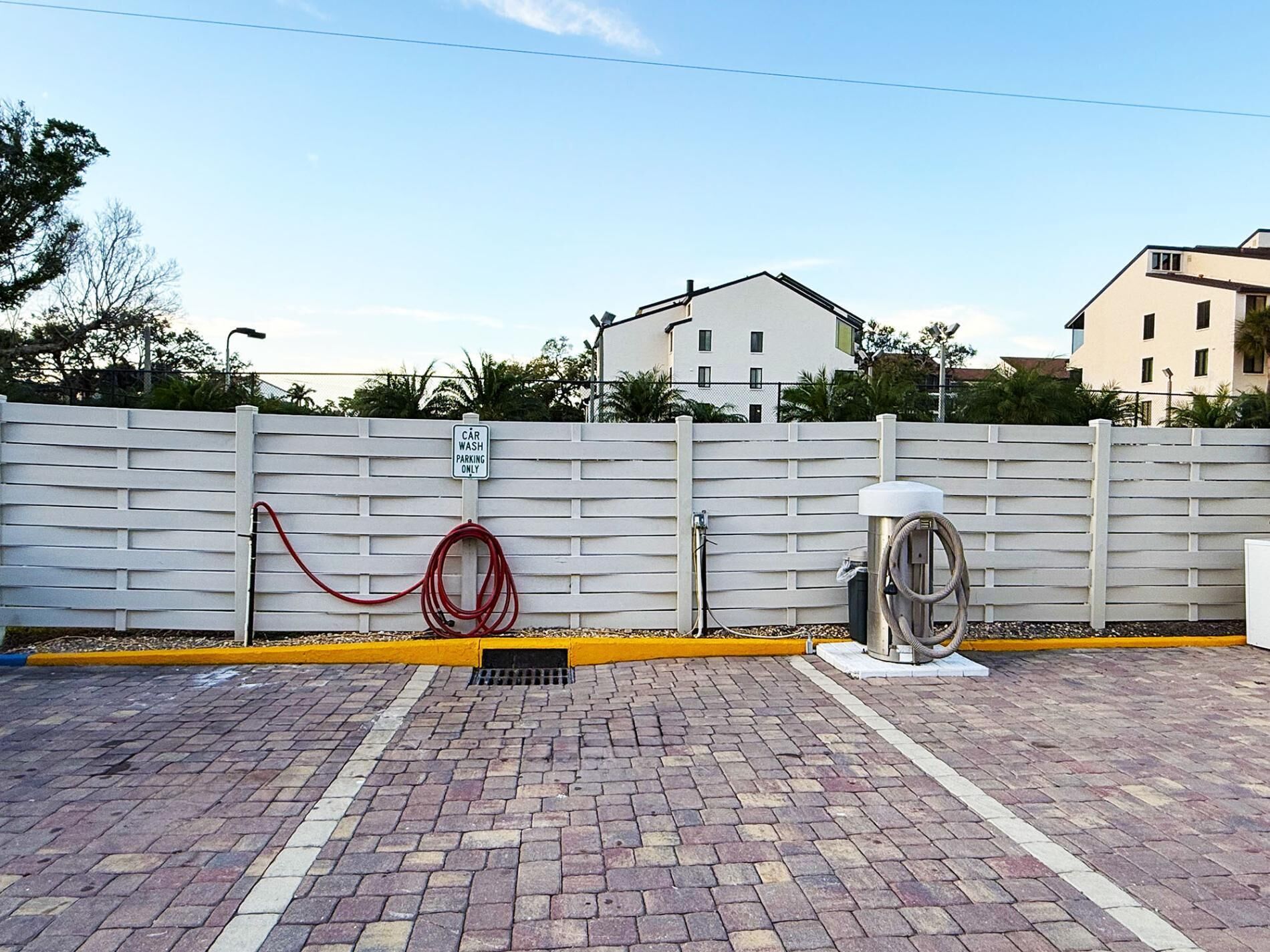 Un poste de lavage automobile équipé d’un tuyau d’arrosage et d’une pompe à eau, ainsi qu’une zone délimitée par une clôture et des bâtiments en arrière-plan.