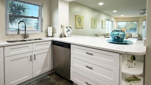 Een moderne keuken met witte kastjes, een vaatwasser en een groot eiland met een blauwe decoratieve kom.