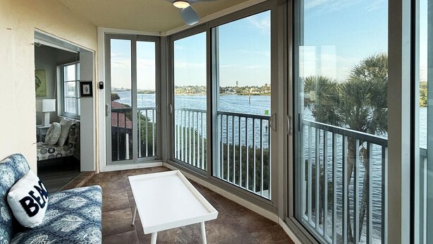 Een balkon met uitzicht op een wateroppervlak, een plafondventilator en een witte tafel.